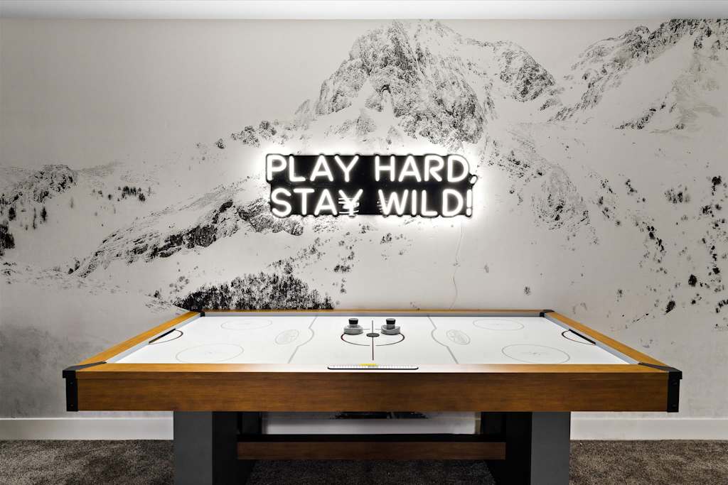 The Evergreen — air hockey table against a mountain wall mural with an illuminated neon sign above