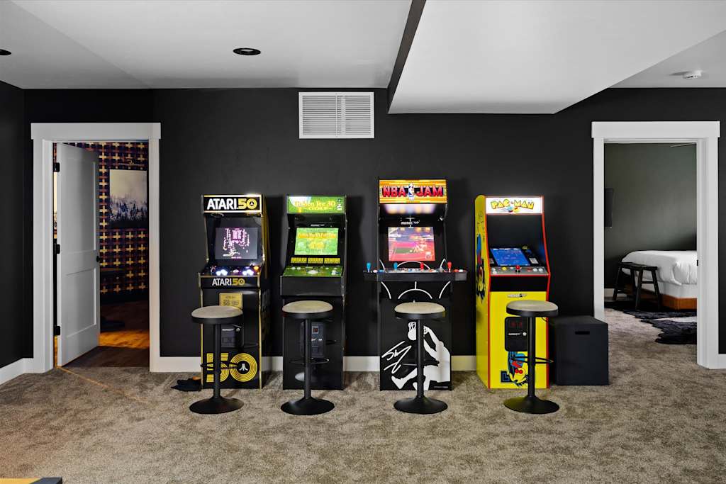 The Evergreen — row of four arcade machines with accompanying barstools against a dark gray wall