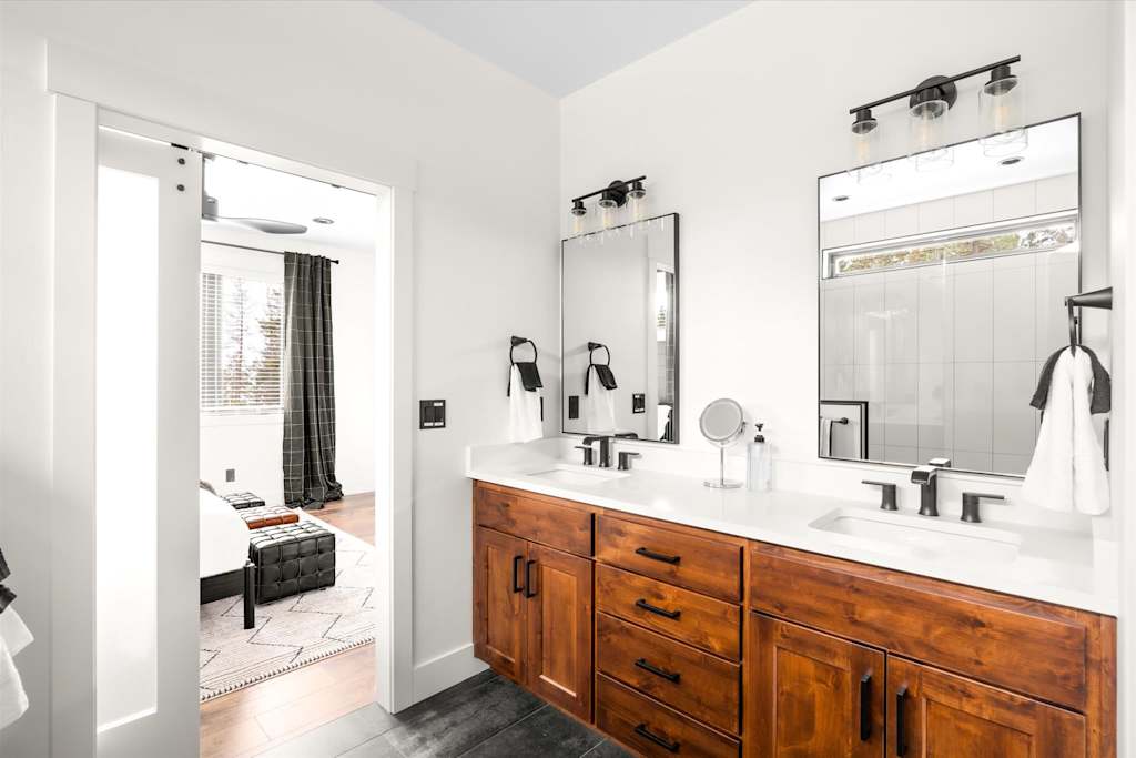 The Evergreen — ensuite bathroom with double sink wood vanity, black fixtures, dual mirrors, and sliding door