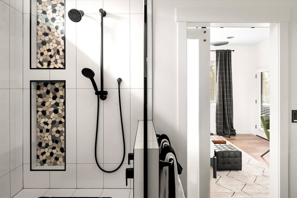 The Evergreen — walk-in shower with white tiles, pebble-inlaid wall niches, and matte black showerhead fixtures