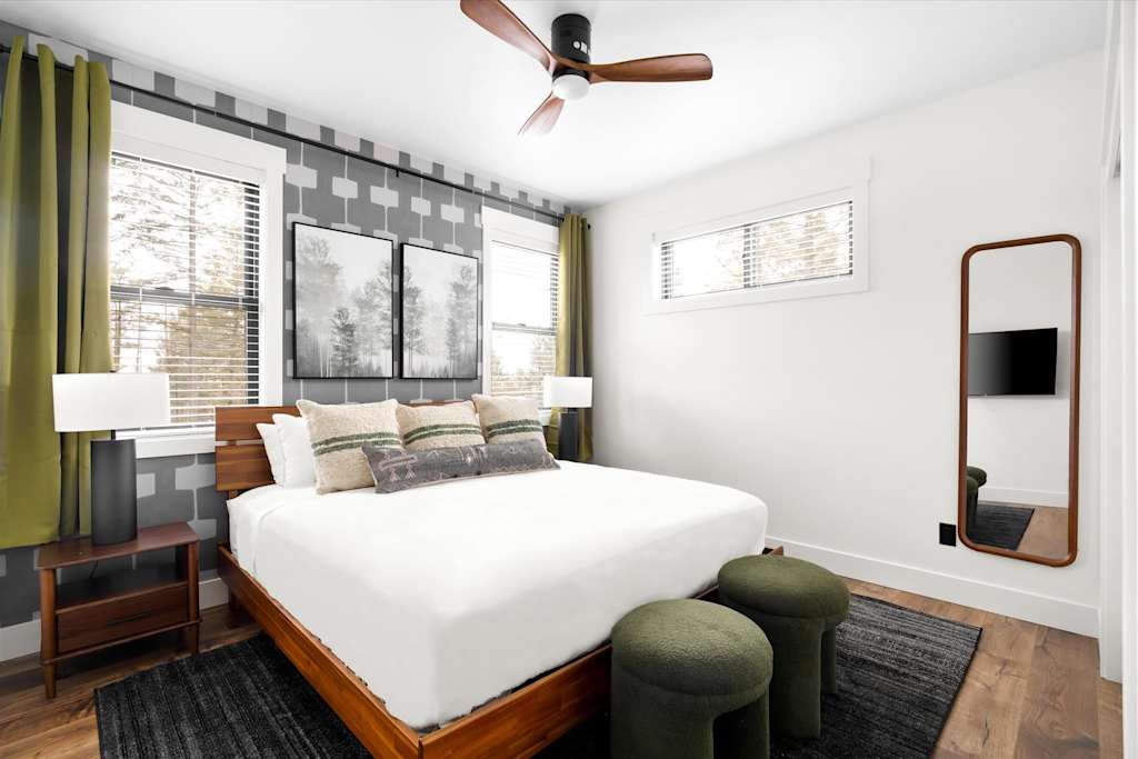 The Evergreen — bedroom with wooden bed, green curtains and ottomans, ceiling fan, and full-length mirror