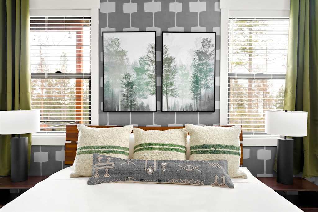 The Evergreen — bedroom with pillows on a bed beneath framed forest art flanked by two windows with lamps