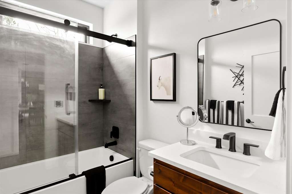 The Evergreen — bathroom featuring a single-sink vanity, mirror, toilet, and bathtub with sliding glass doors