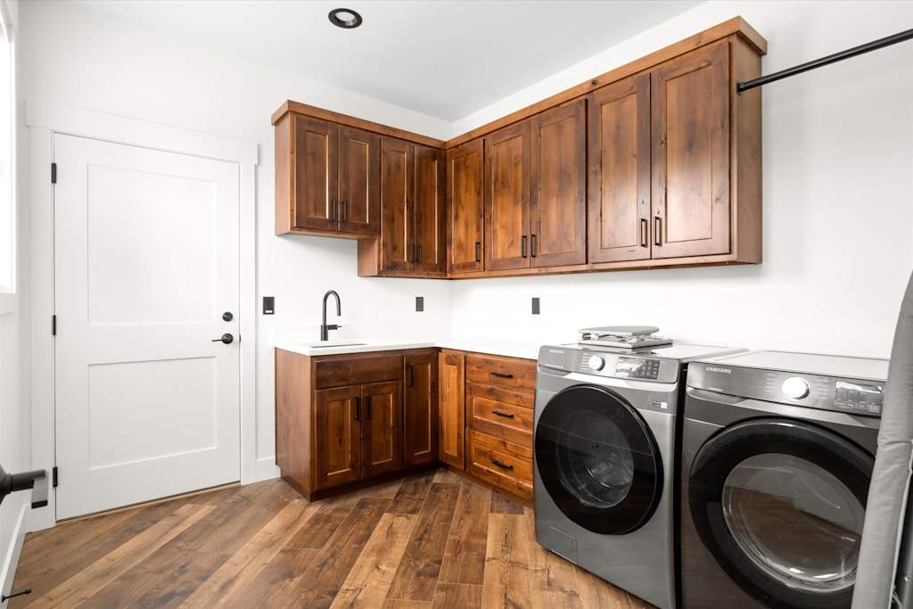 The Evergreen — laundry room with wood cabinetry, a utility sink, and front-loading washer and dryer