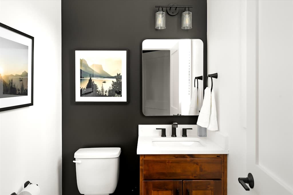 The Evergreen — half bathroom with a black accent wall, wooden vanity, mirror, and toilet