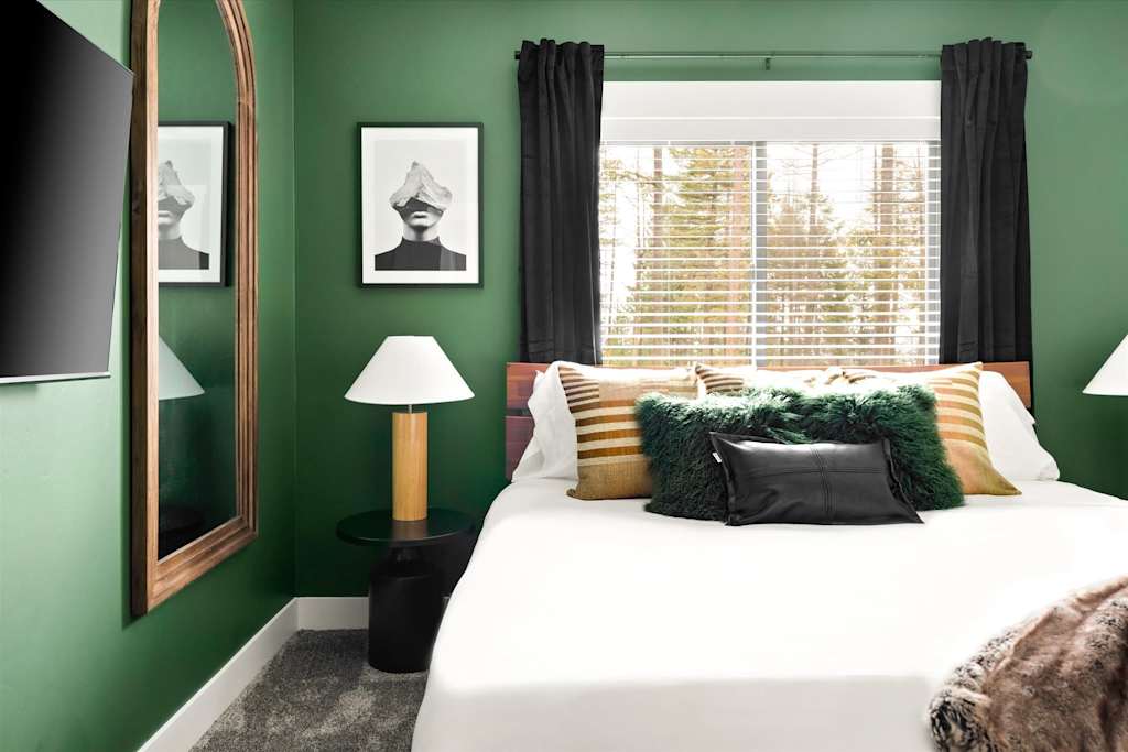 The Evergreen — bedroom with green walls, arched full-length mirror, and bed positioned beneath a window with blinds