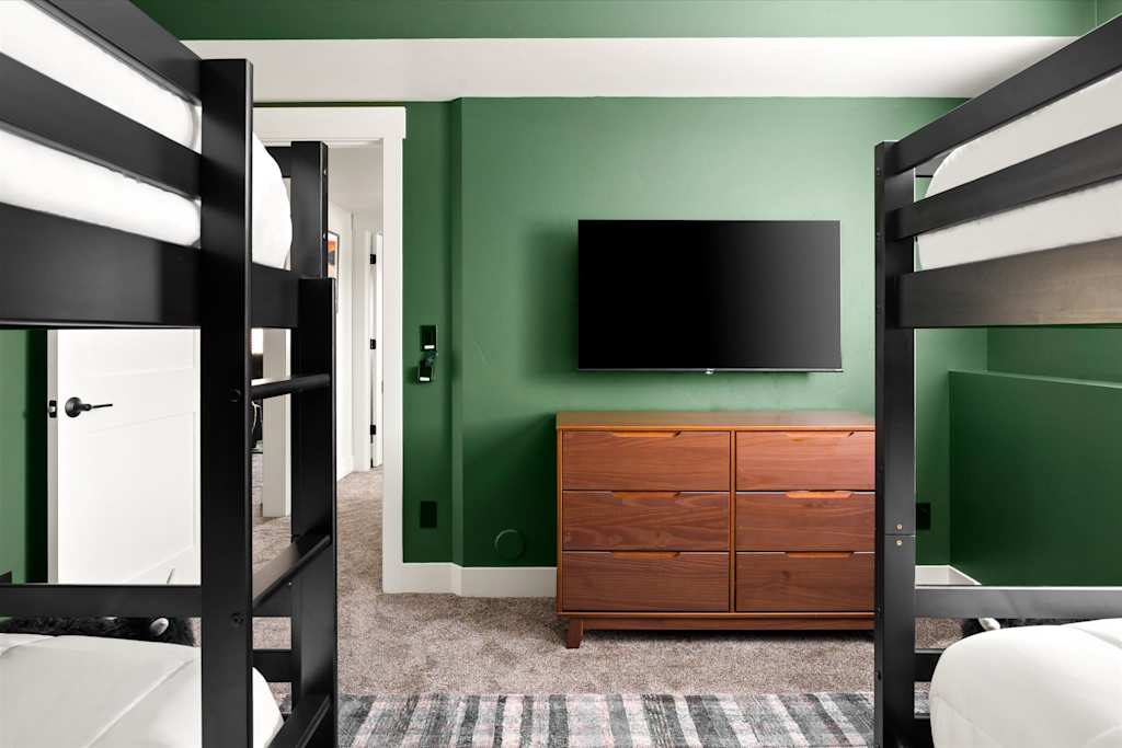 The Evergreen — bunk bedroom featuring a wooden dresser and wall-mounted tv between two bunk bed sets