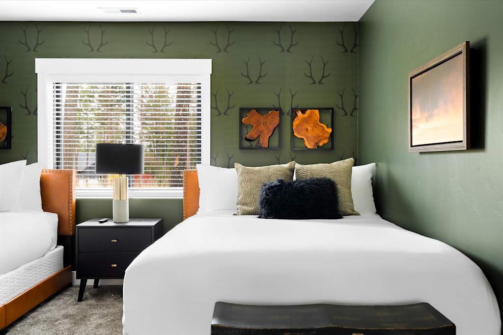 The Evergreen — bedroom with antler-patterned accent wall, nightstand with lamp, and bed with white linens