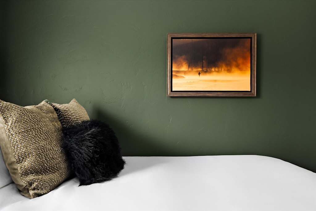 The Evergreen — bed with decorative textured pillows against a dark green wall beneath framed artwork