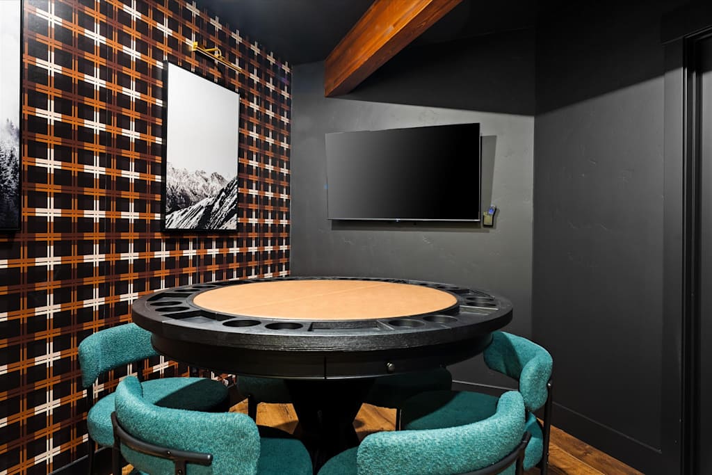 The Evergreen — poker table surrounded by teal chairs in a room with plaid wallpaper and a wall-mounted tv