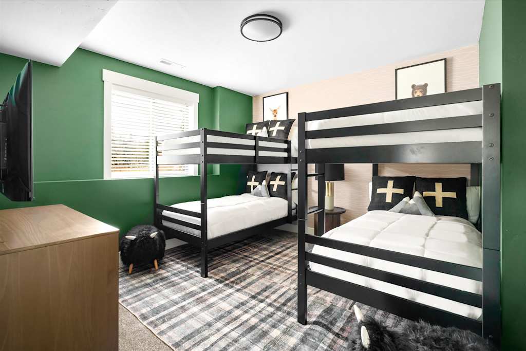 The Evergreen — bunk bedroom featuring two black bunk beds, green walls, and a plaid area rug