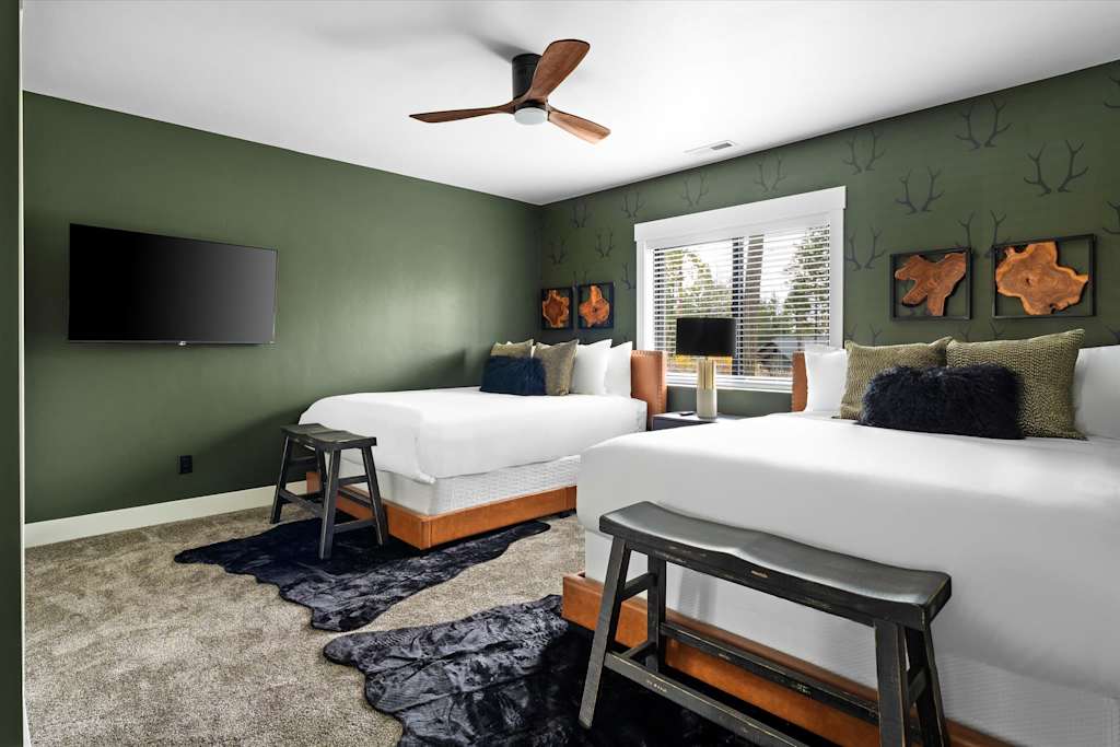 The Evergreen — bedroom with two beds, wooden end benches, green walls with antler patterns, and a ceiling fan