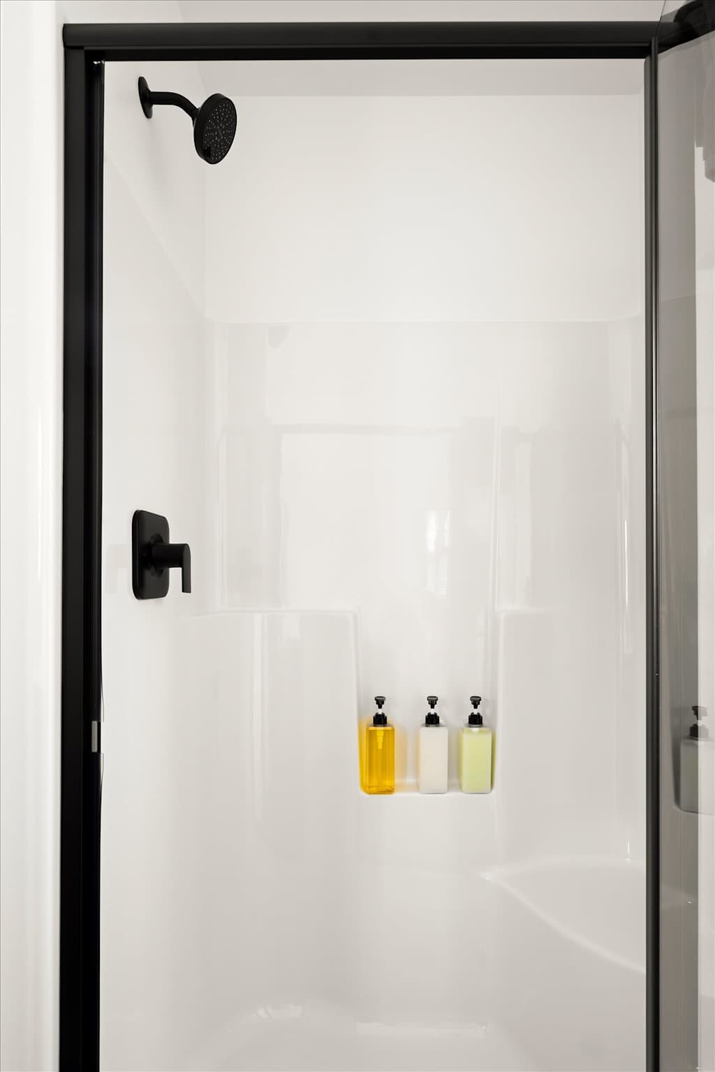 The Evergreen — white walk-in shower enclosure with black hardware and three pump bottles in a built-in shelf