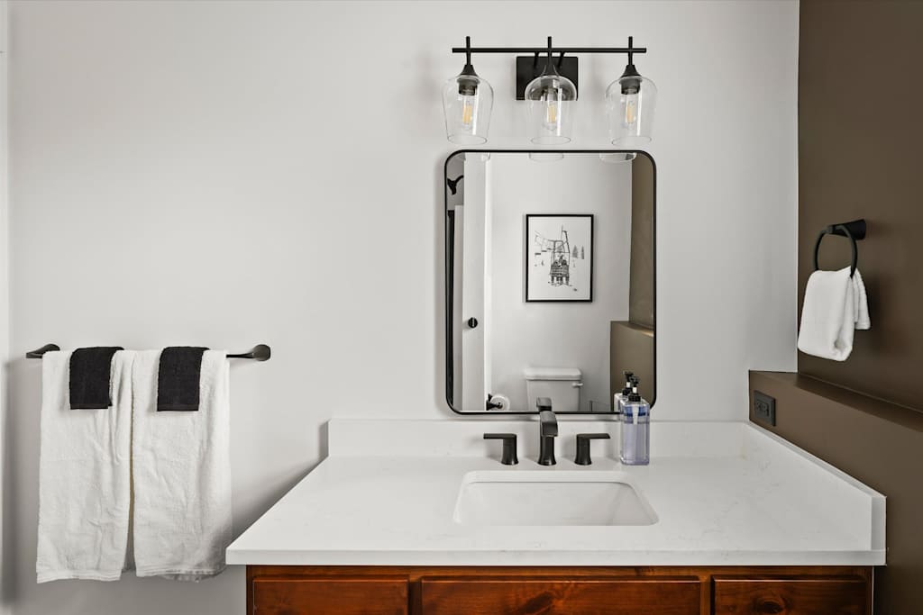 The Evergreen — bathroom vanity with a white countertop, wood vanity base, black faucet, and rectangular mirror