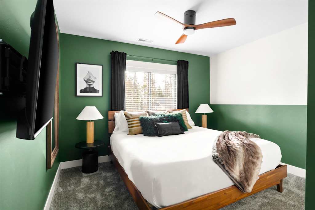 The Evergreen — bedroom with a wood-frame bed, green walls, bedside lamps, ceiling fan, and mounted tv