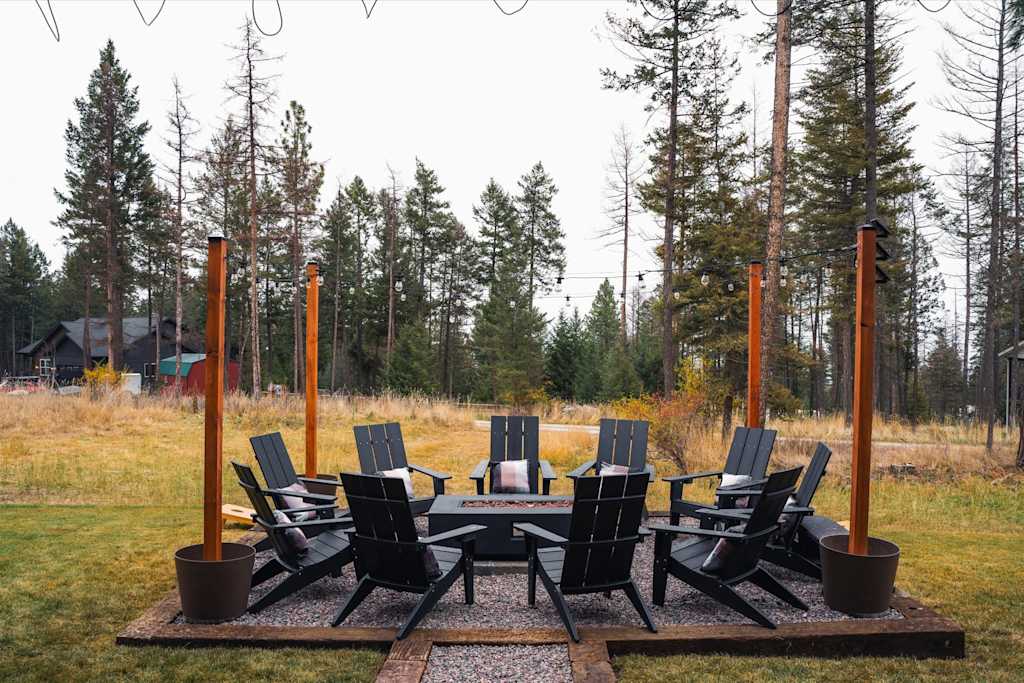 The Evergreen — circular arrangement of black adirondack chairs around a fire pit on a gravel patio with trees
