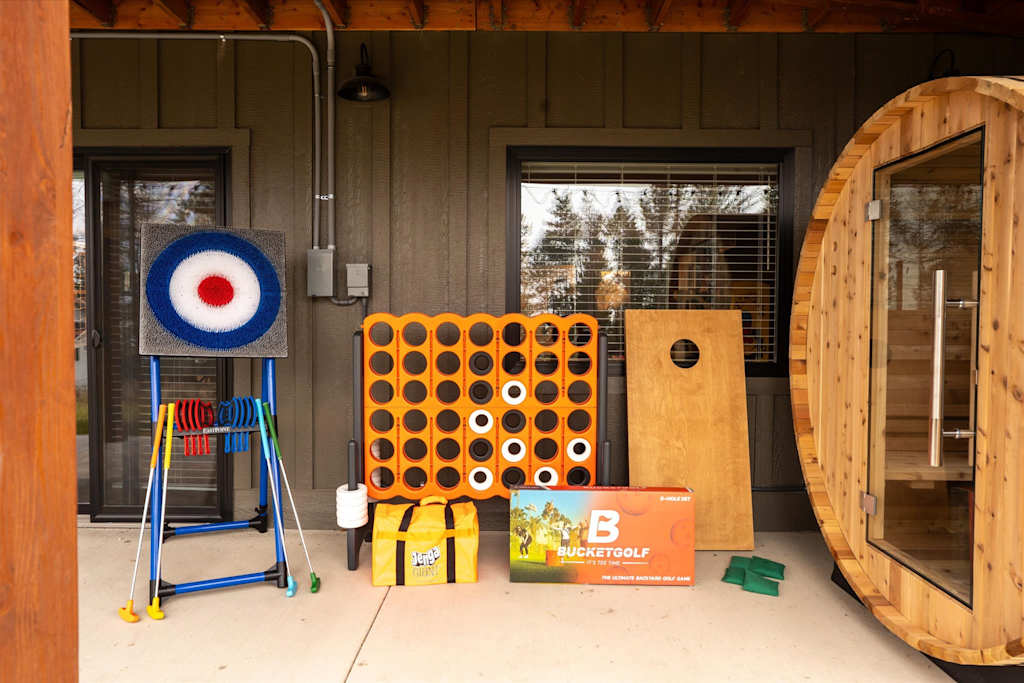 The Evergreen — outdoor games collection including giant four-in-a-row, target toss, and cornhole beside a barrel sauna
