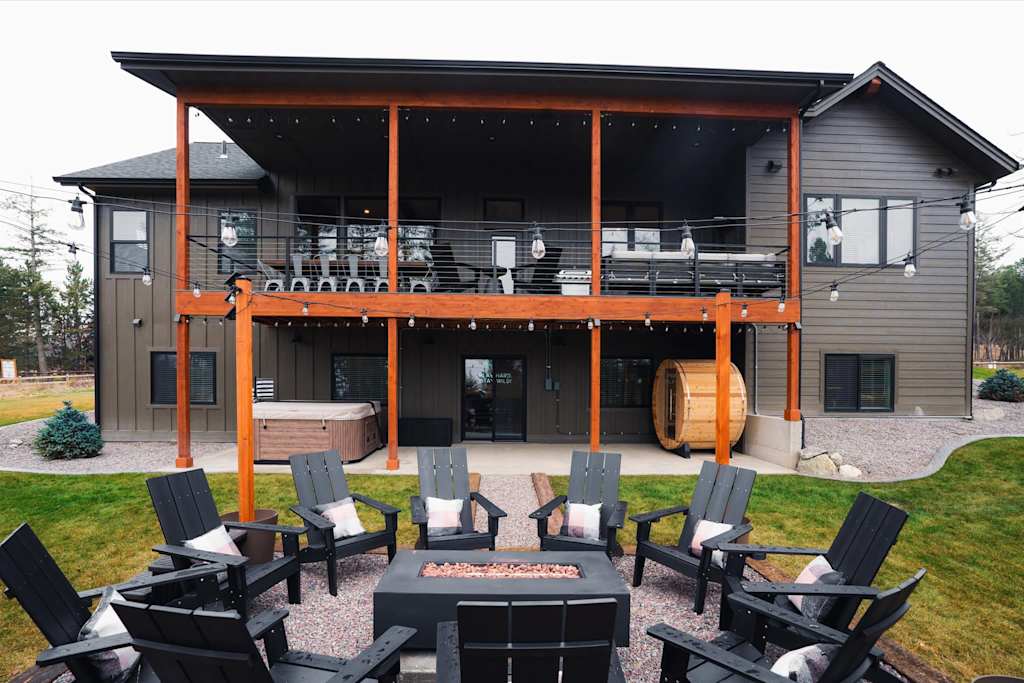 The Evergreen — back patio with black chairs around a fire pit, covered porch, hot tub, and barrel sauna