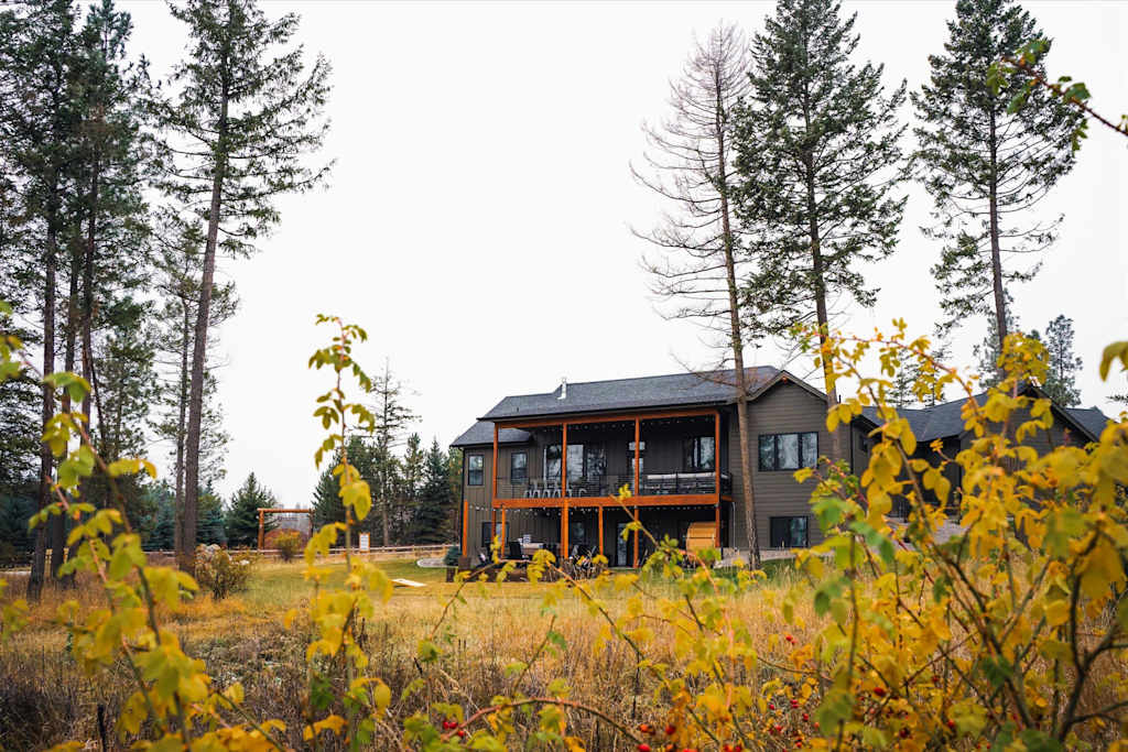 The Evergreen — distant view of a two-story house surrounded by pine trees, viewed through yellow foliage
