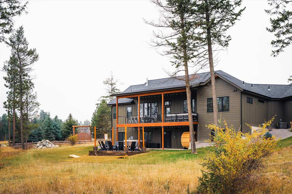 The Evergreen — backyard view of house showing two-story deck, fire pit seating area, and grassy lawn