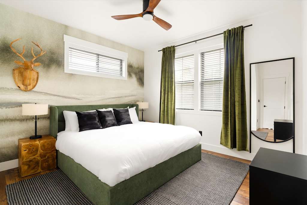 The Evergreen — bedroom with a large bed, green headboard, wooden nightstand, deer antler decor, and large mirror