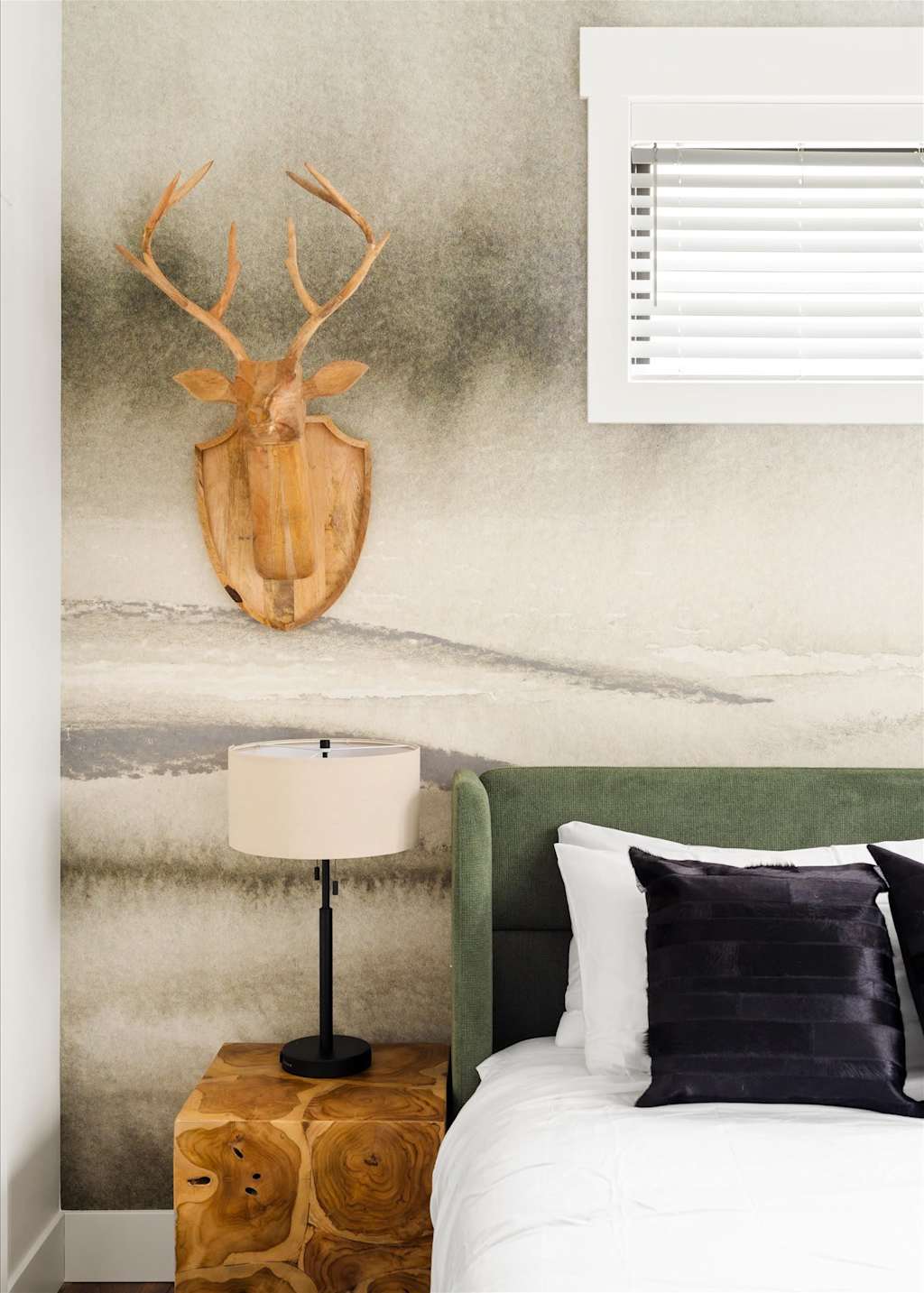 The Evergreen — close-up of a carved wooden deer head above a bedside table and green headboard