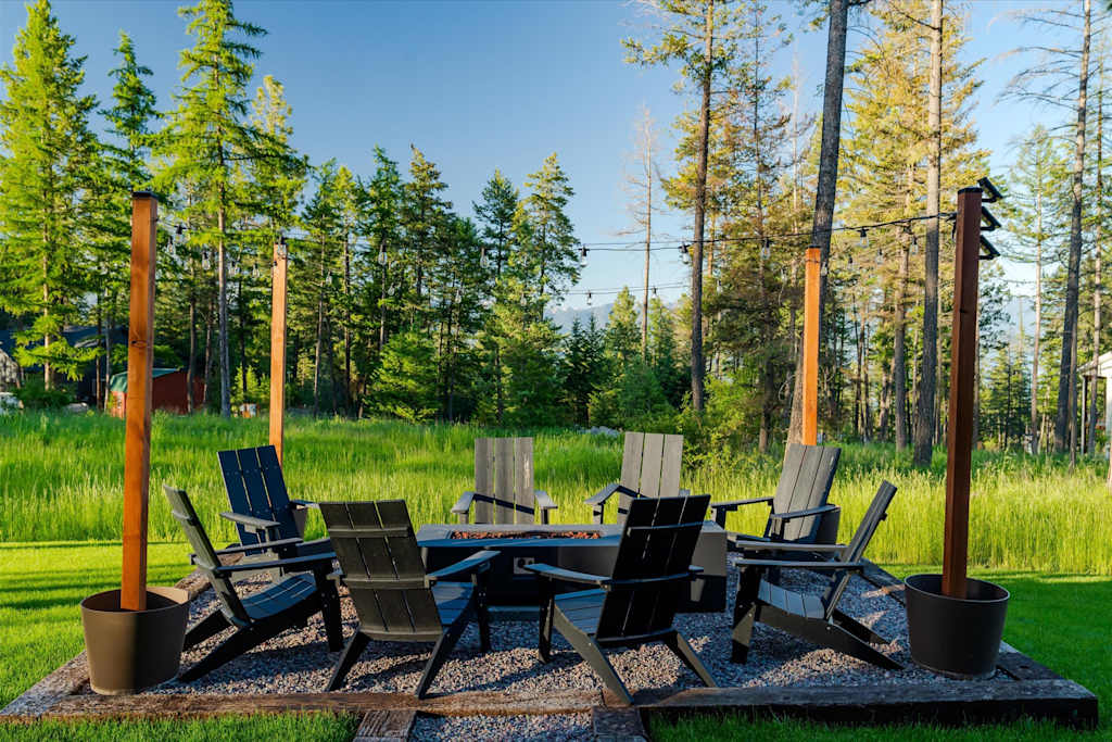The Evergreen — outdoor gravel fire pit with black adirondack chairs surrounded by green lawn and trees