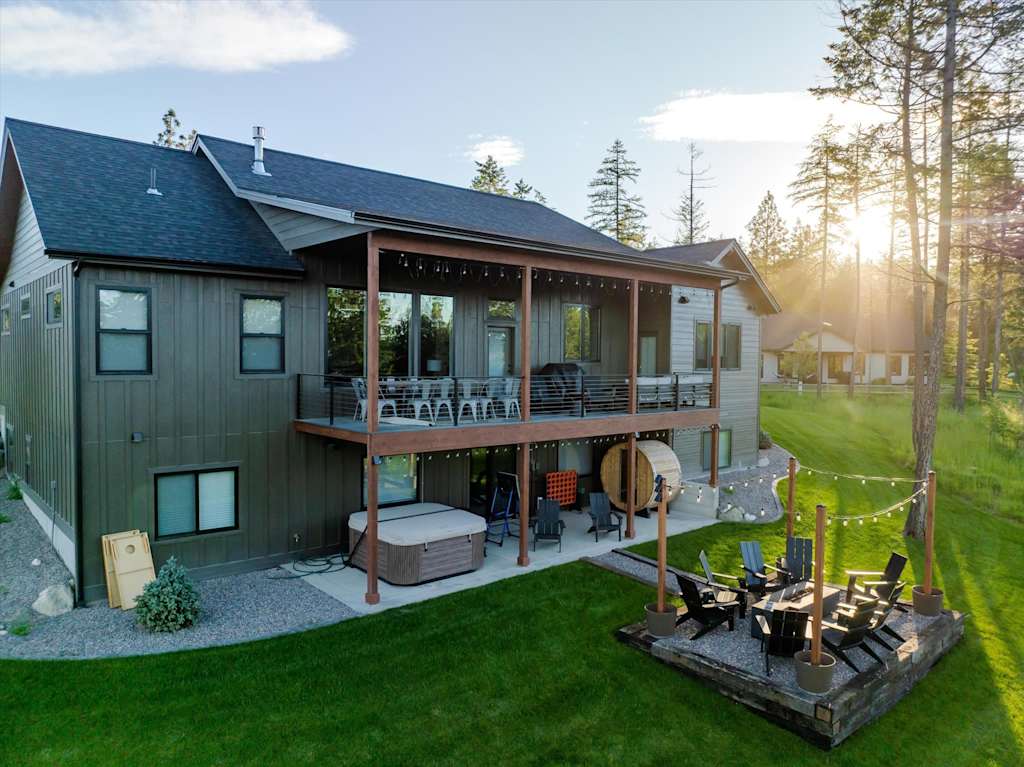 The Evergreen — back view of house with covered deck, hot tub, barrel sauna, and outdoor fire pit patio