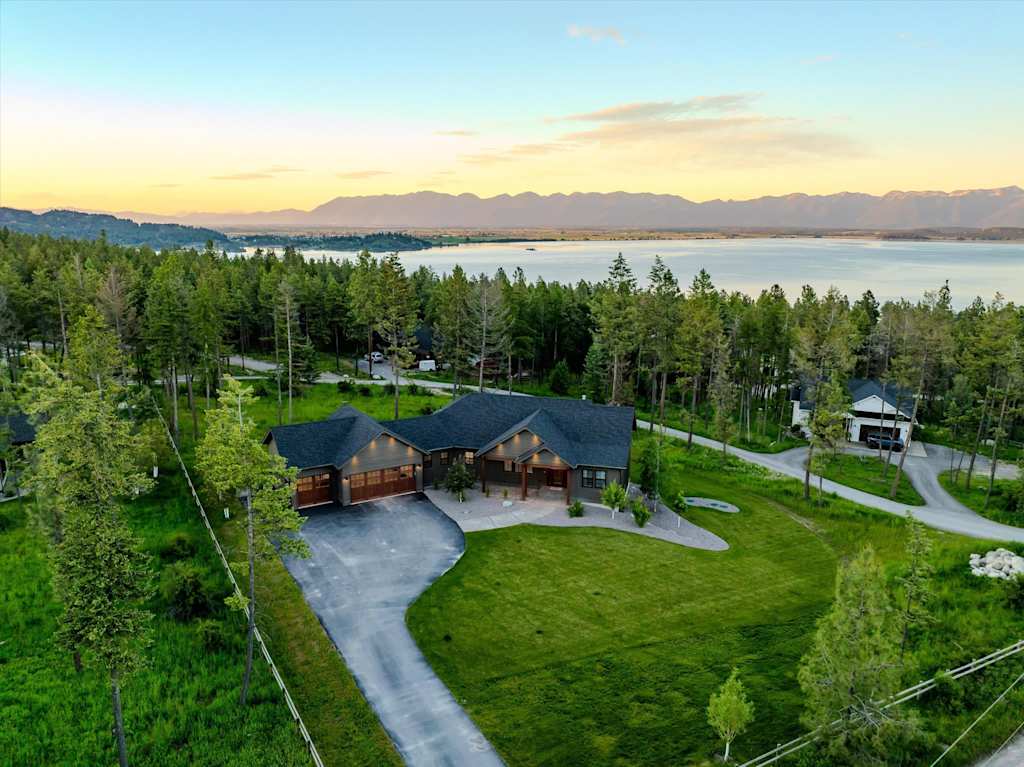The Evergreen — aerial view of the house and driveway surrounded by forest with a lake and mountains behind