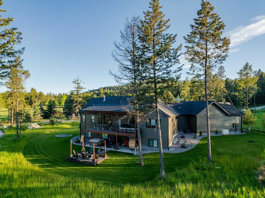 The Evergreen — rear exterior view of the house, lawn, deck, and fire pit framed by tall pine trees