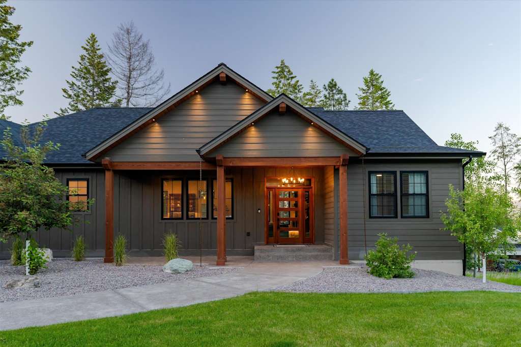 The Evergreen — front porch and entrance of the house with dark siding, wooden posts, and lighted glass door