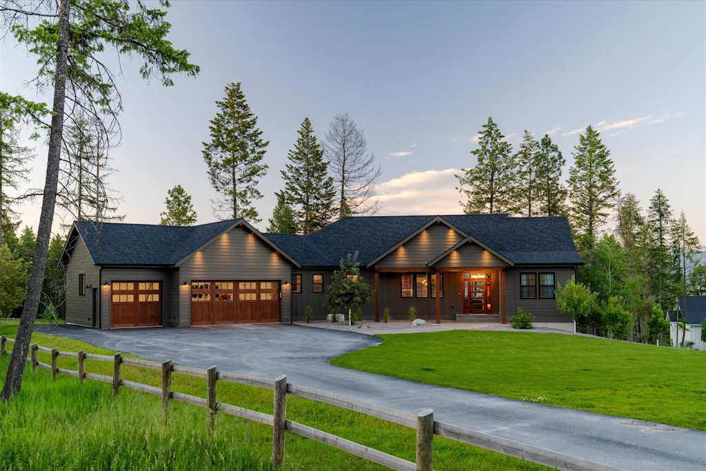 The Evergreen — front exterior of the house featuring a paved driveway, attached garage, front porch, and split-rail fence