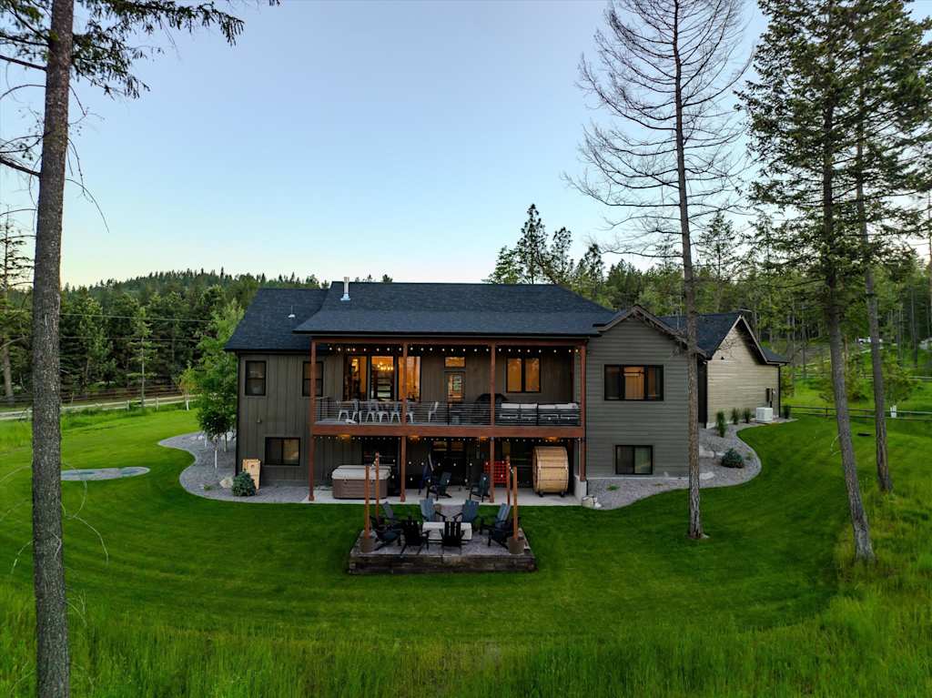 The Evergreen — straight-on view of the back of the house with covered deck, patio fire pit, and lawn