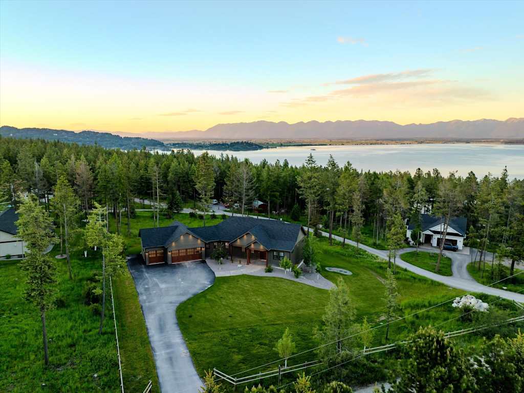 The Evergreen — aerial view of a house nestled in trees with a large lake and mountains in the background