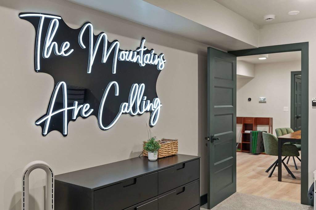 The Tamarack — dresser with a neon sign reading the mountains are calling mounted on the wall