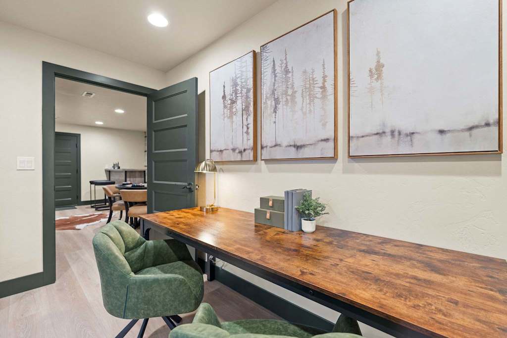 The Tamarack — wooden desk with green chairs beneath three framed forest landscape prints