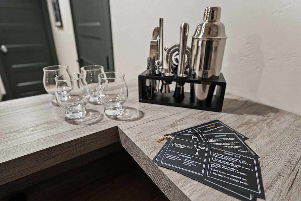 The Tamarack — cocktail shaker set, glasses, and cocktail recipe cards on a wooden bar counter