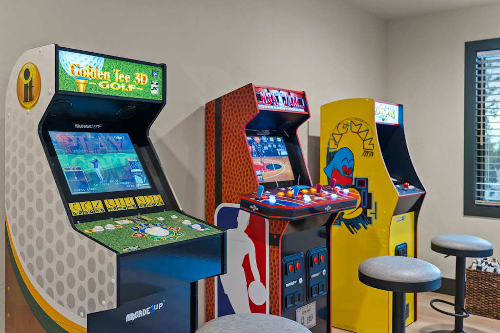 The Tamarack — row of three arcade game cabinets with barstools in an entertainment room