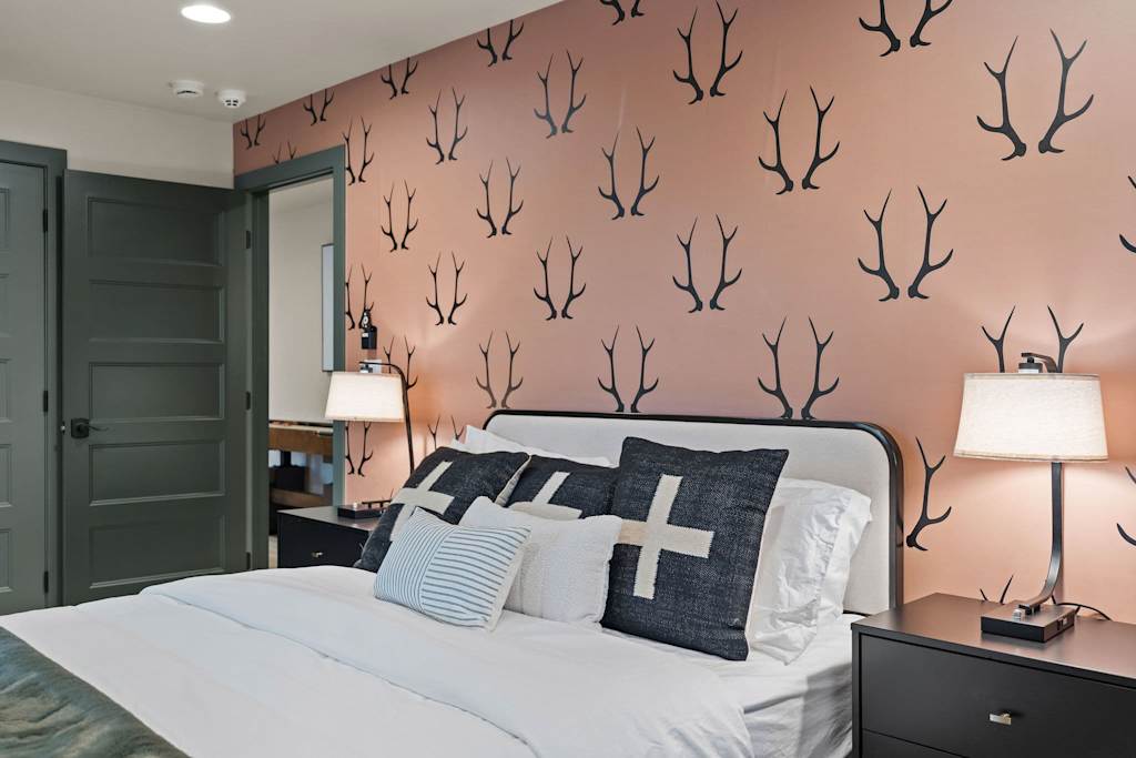 The Tamarack — bedroom with antler pattern wallpaper, bed with decorative pillows, and nightstands with lamps