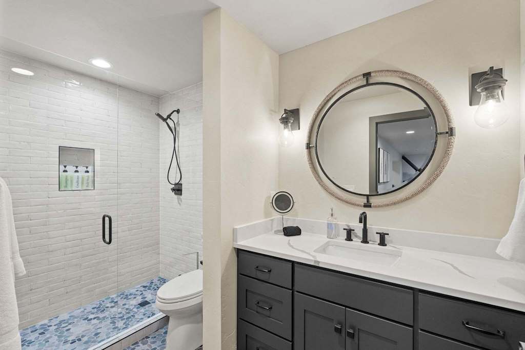 The Tamarack — bathroom featuring a dark vanity, round mirror, and a glass-enclosed walk-in shower