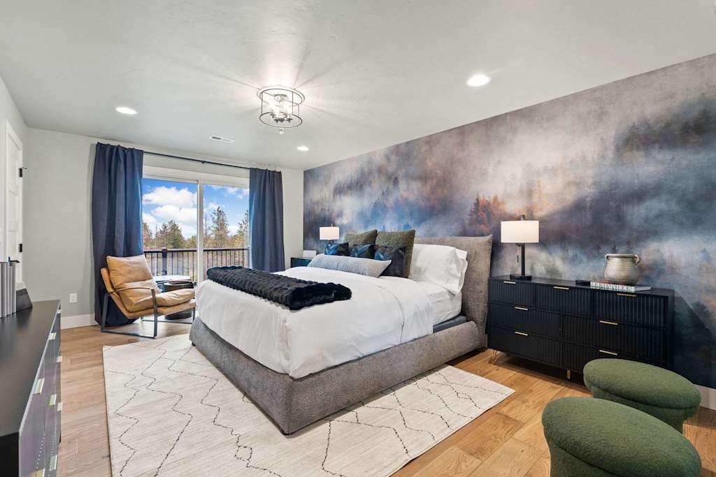 The Tamarack — bedroom with a large bed, forest mural accent wall, black dresser, armchairs, and balcony doors