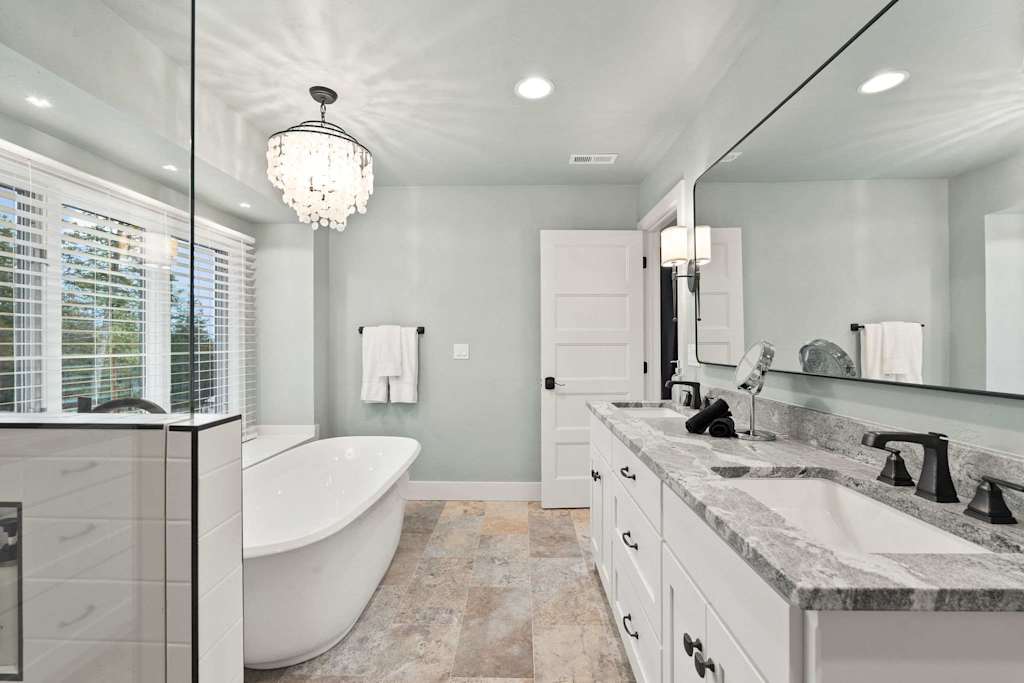 The Tamarack — bathroom featuring a double vanity, white freestanding bathtub, large mirror, and chandelier