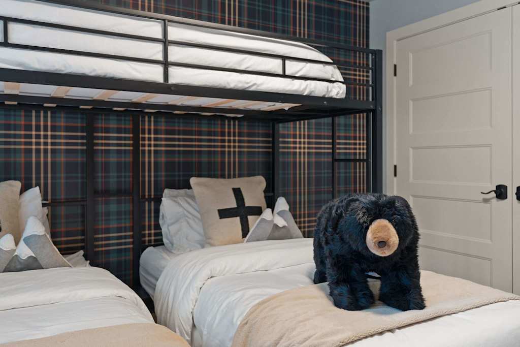 The Tamarack — bunk room with plaid wallpaper, metal bunk beds, and a plush black bear on the bed
