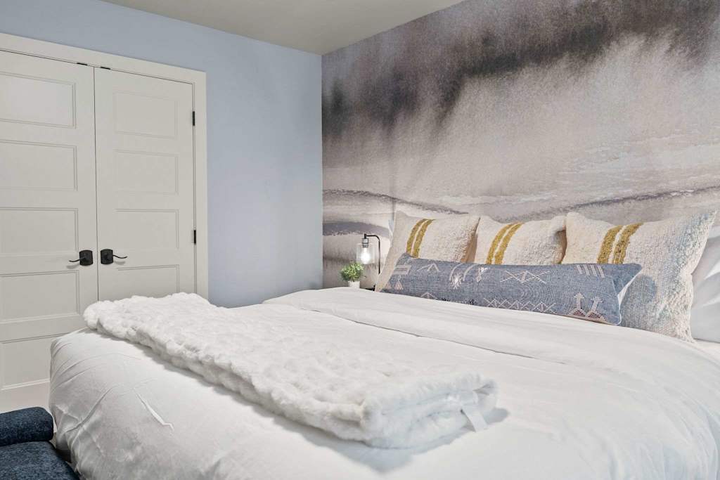 The Tamarack — bed with white linens and decorative pillows set against an abstract wall mural
