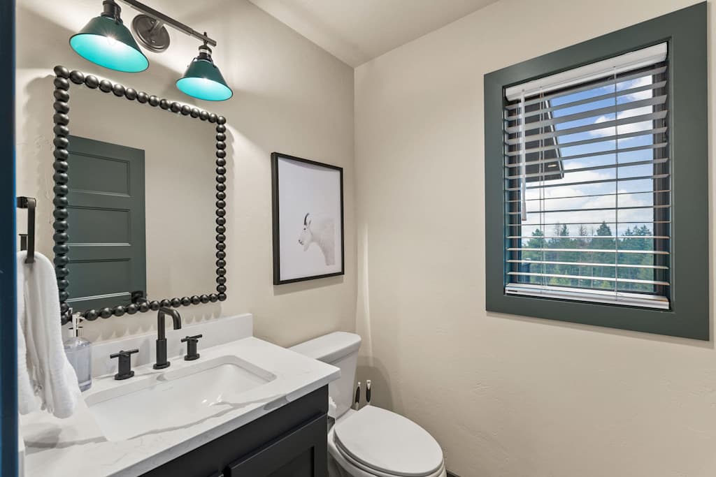 The Tamarack — bathroom vanity with black beaded mirror, toilet, and a window with blinds