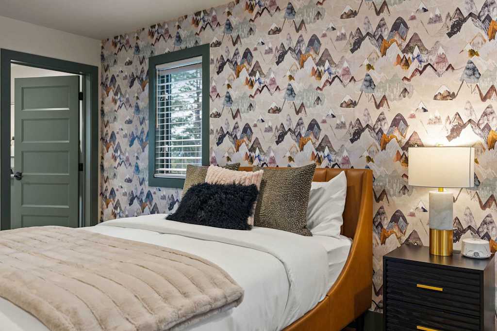 The Tamarack — bedroom with mountain patterned wallpaper, leather bed frame, and nightstand with lamp