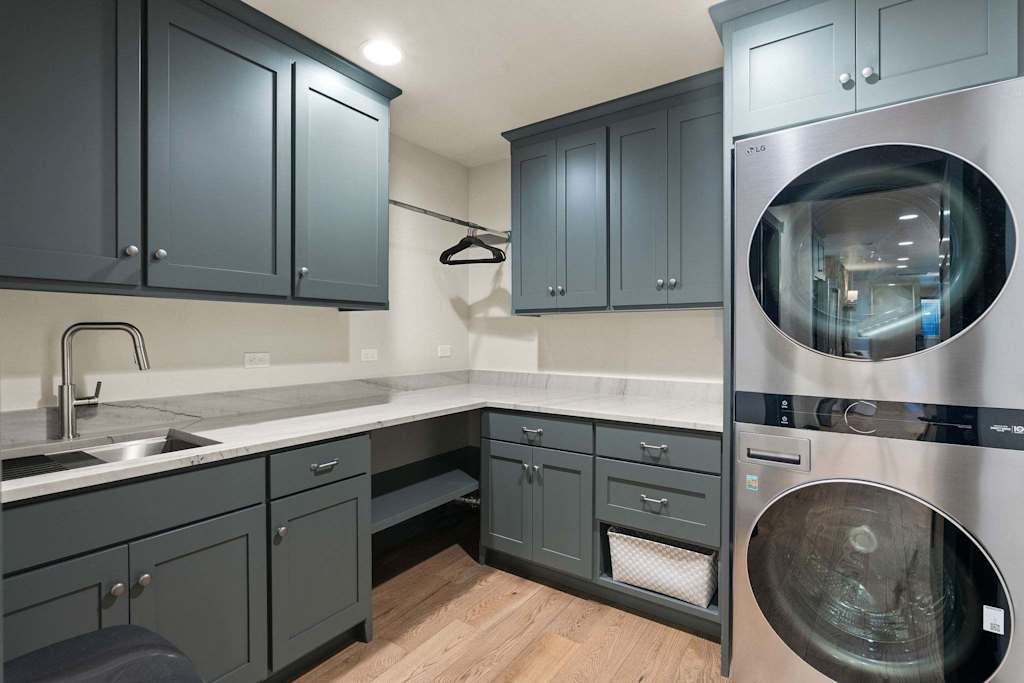 The Tamarack — laundry room with gray cabinets, countertops, sink, and stacked stainless steel washer and dryer