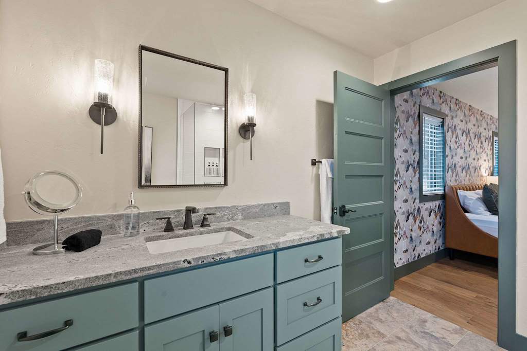 The Tamarack — bathroom vanity with granite countertop and mirror, looking through open doorway into a bedroom