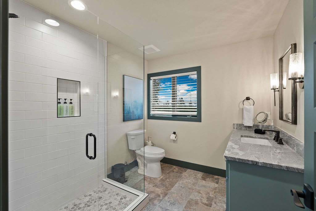 The Tamarack — bathroom with a glass-enclosed walk-in shower, toilet, window, and granite-top vanity