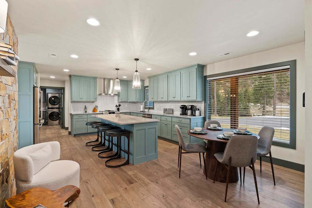 The Tamarack — open kitchen and dining area with blue-green cabinetry, kitchen island, and round dining table